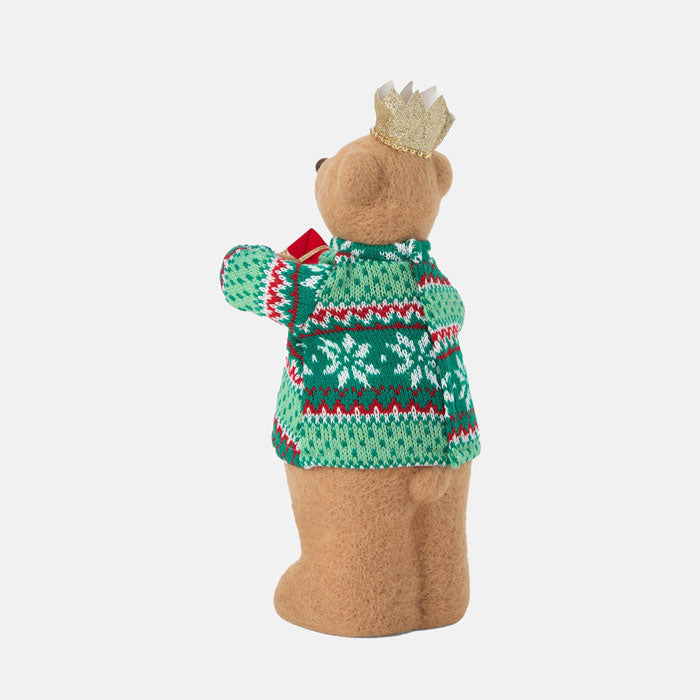 Teddy bear wearing a green sweater with red patterns and a gold crown on a white background