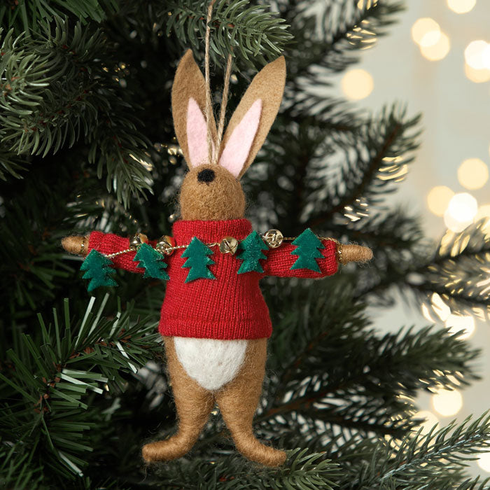 Felt rabbit ornament wearing a red sweater with green trees on a Christmas tree.