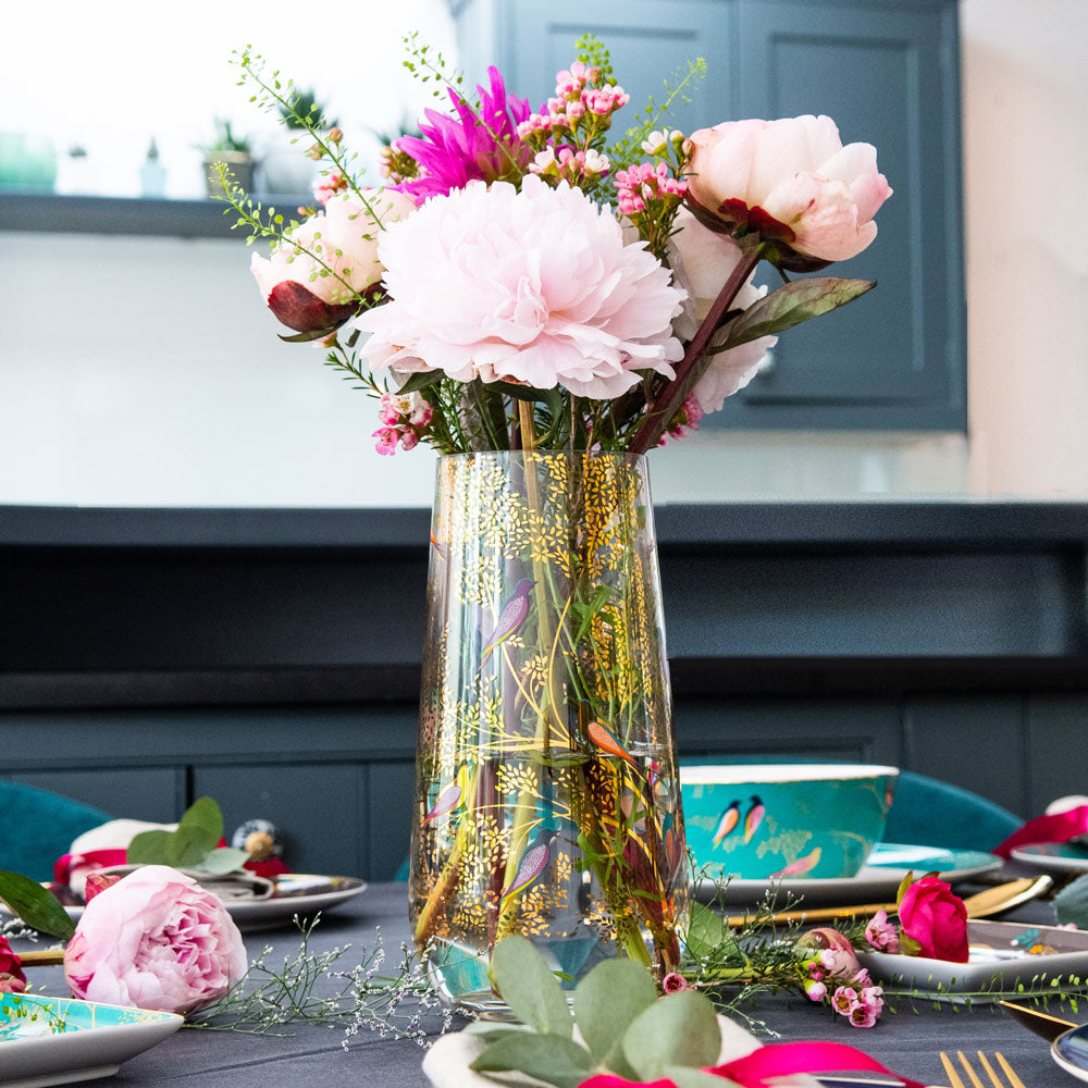 Vase shown with flowers inside on table setting, can see stems inside clear vase.