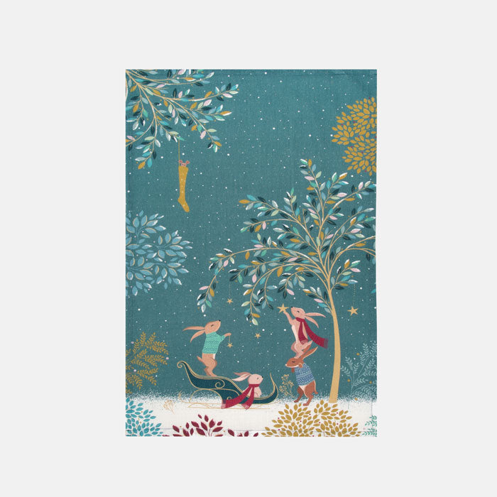A festive tea towel featuring woodland rabbits decorating the woodland for the season, against a starry sky on a soft blue background.