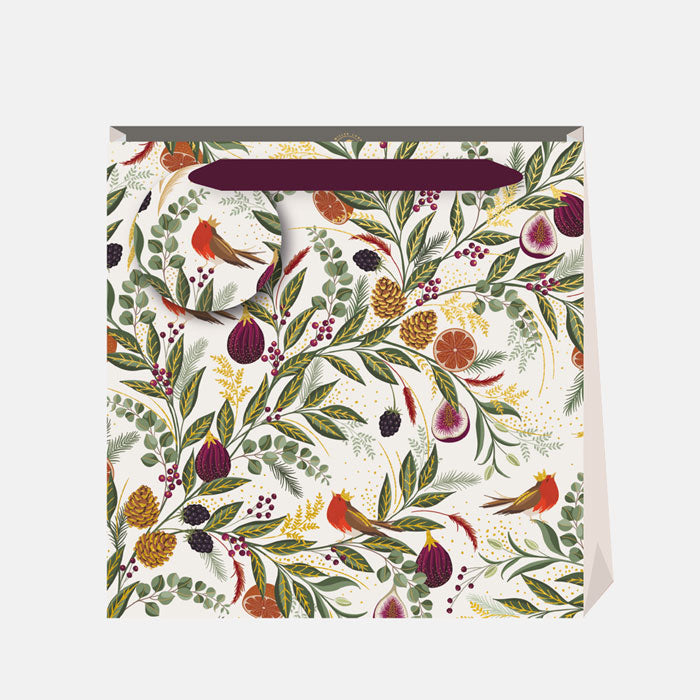 A Christmas gift bag with winter foliage, figs and robins in greens and reds on a cream base, with matching gift tag and ribbon handles.
