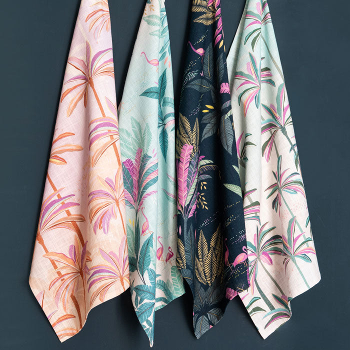 Four tea towels from the same collection hanging against a dark background.
