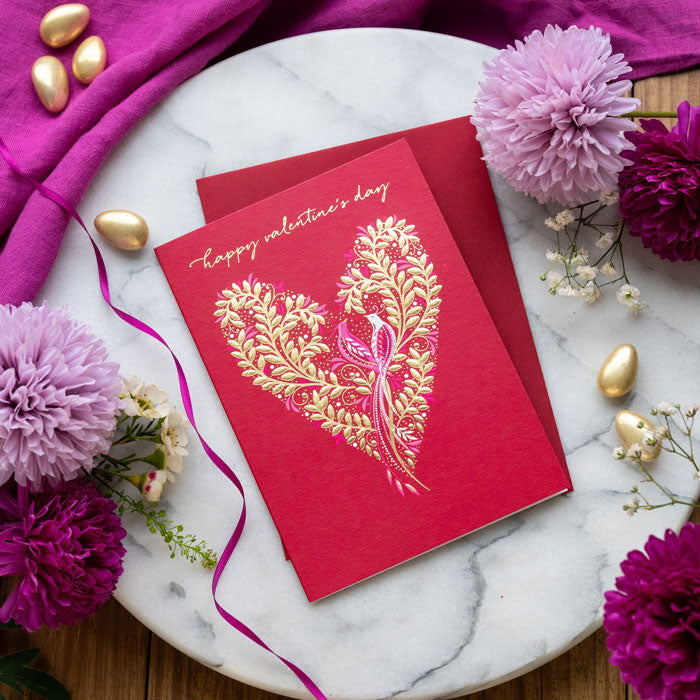 Valentine's Day card with gold heart design on a marble surface with flowers and ribbons.