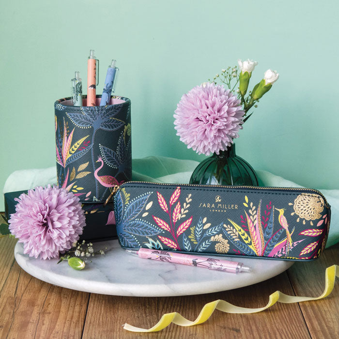 Pencil case with floral design on blue background on a marble tray with flowers and pens, against a light green backdrop.