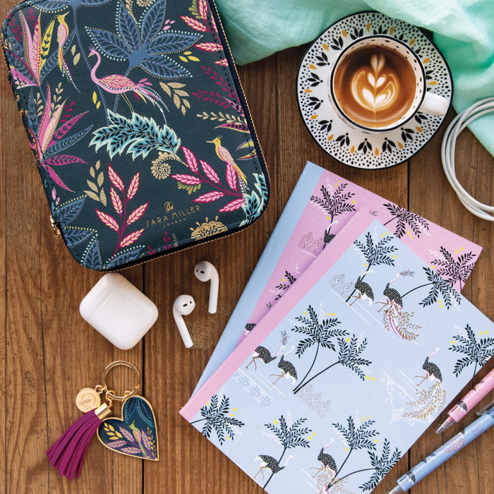 Floral patterned case, notebooks, coffee, earbuds, keychain on a wooden surface