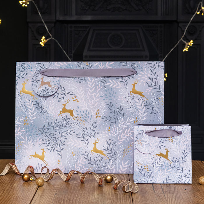 Two Sara Miller London gift bags with deer pattern on a wooden surface.