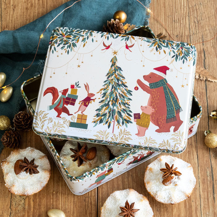 Decorative Christmas tin with festive illustrations on a wooden surface with mince pies.