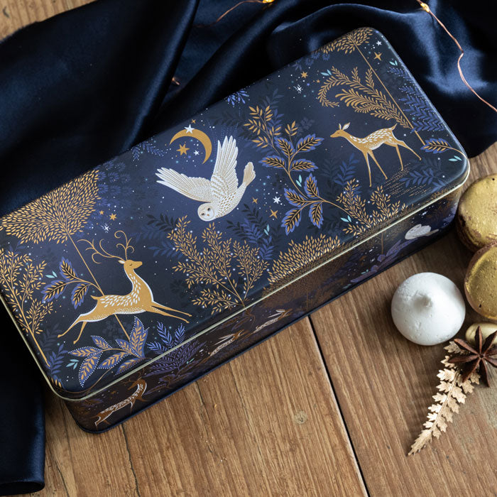 Decorative tin box with moonlit forest design on a wooden surface