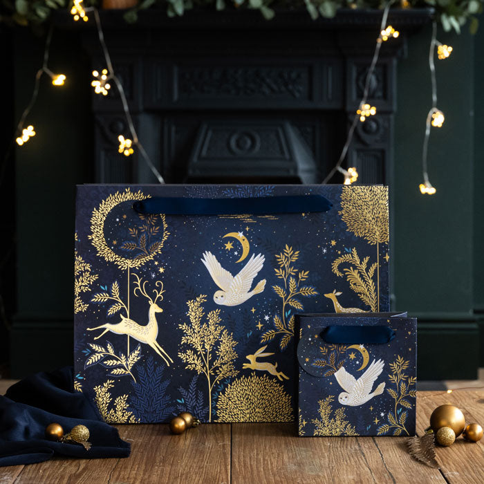 Decorative gift bags with gold animal and nature patterns on a wooden surface with a dark background.