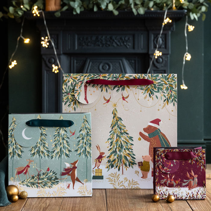 Christmas-themed gift bags with festive designs in front of a fireplace.