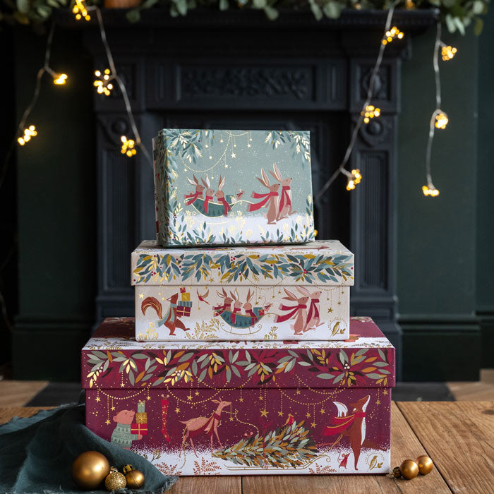 Decorative Christmas boxes with festive designs stacked in front of a fireplace.
