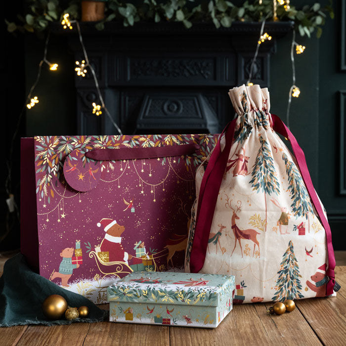 Decorative gift bag, box, and drawstring bag on a wooden surface with a festive background.