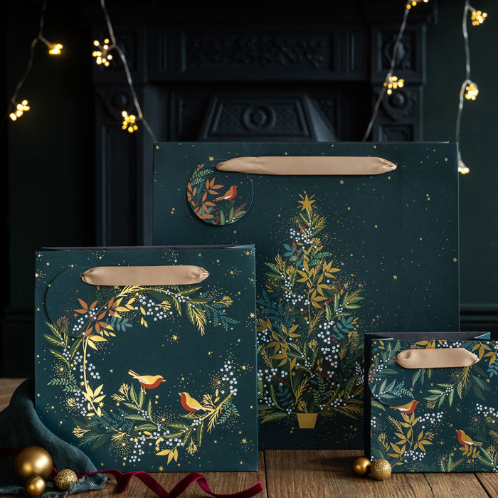 Decorative gift bags in dark green with festive designs on a wooden surface.