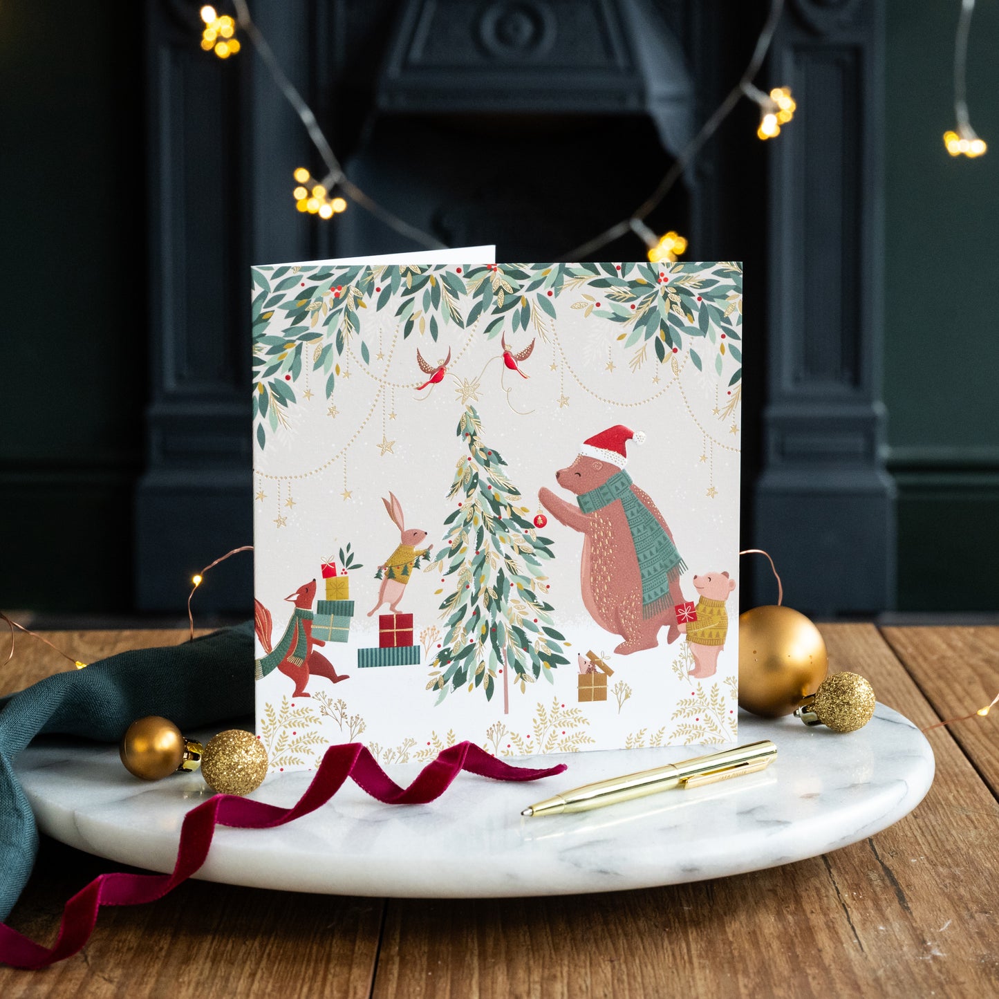 Christmas card with festive illustrations of animals around a tree on a marble surface with decorative items.