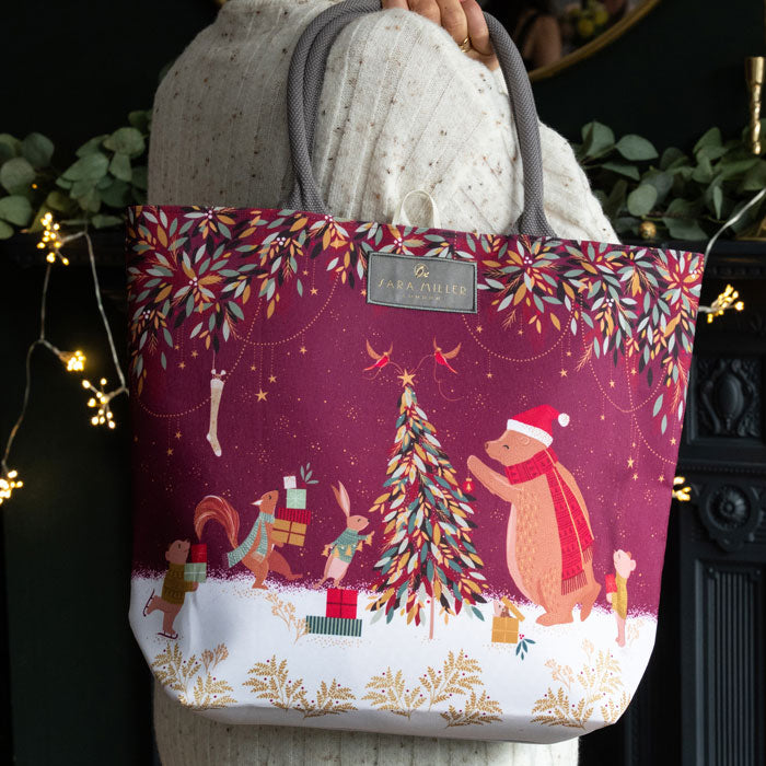 Tote bag with Christmas design featuring a bear and tree, held by a person.