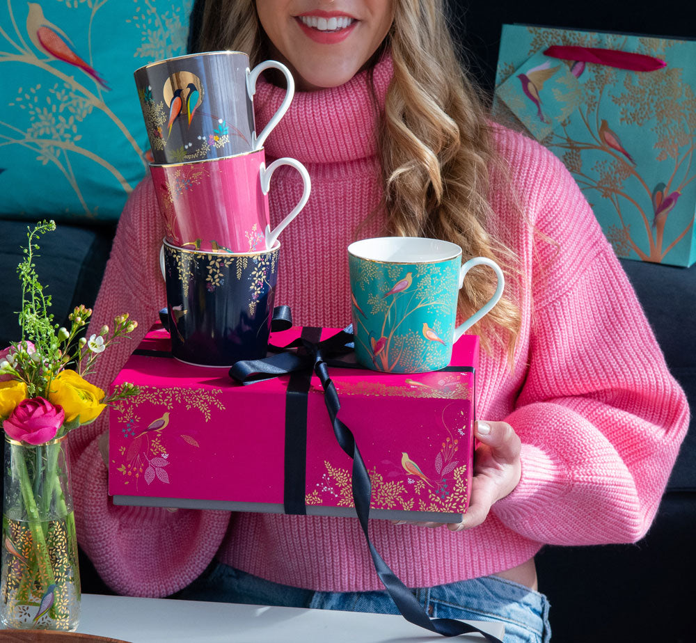 Model holding four mugs stacked on pink packaging box, wrapped with ribbon.