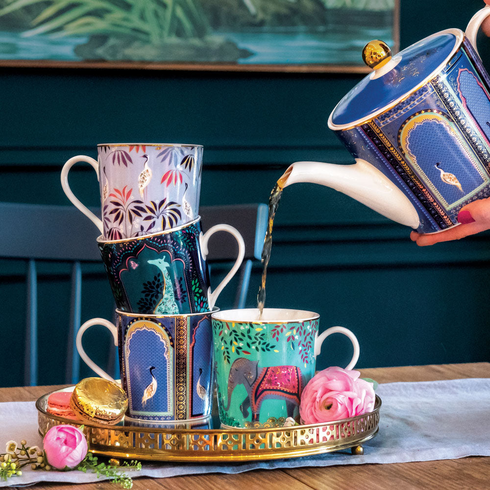 Set of four mugs from the India Collection all in shades of green, blue and pink with gold embellishment, with tea pouring from matching teapot.