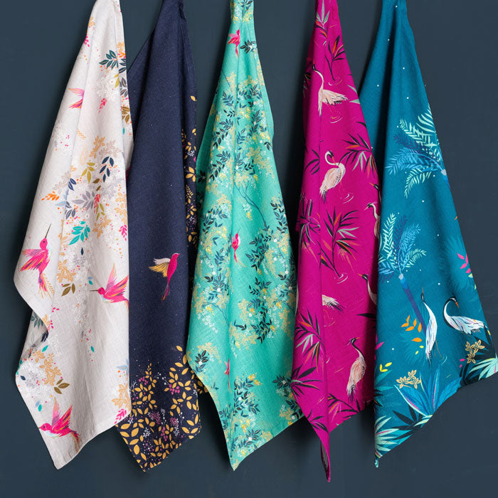 Five tea towels with floral and nature-themed prints hanging against a dark background.