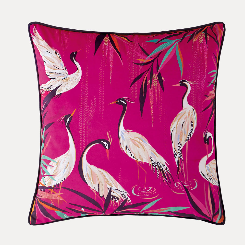 A pink velvet cushion with a pattern of white herons among bamboo flora.