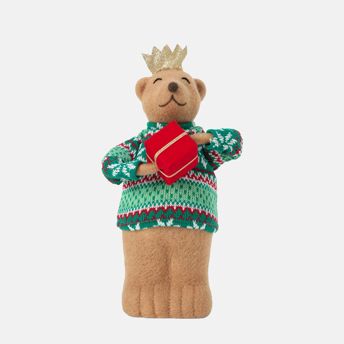 Teddy bear wearing a green sweater with red patterns and a gold crown, holding a red book on a white background.