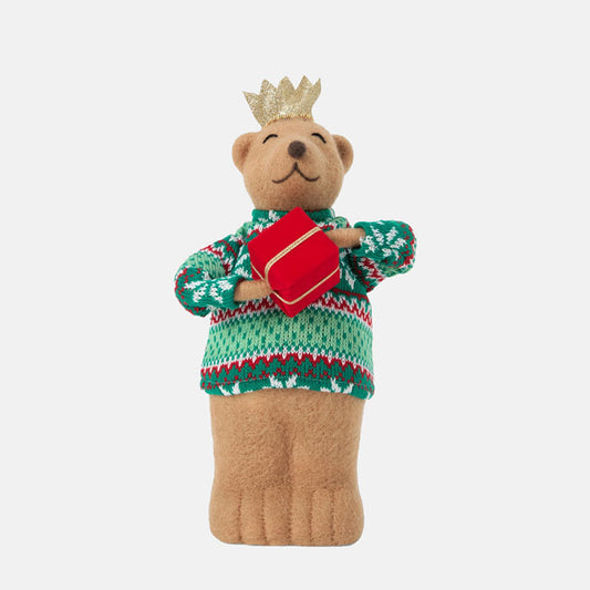 Teddy bear wearing a green sweater with red patterns and a gold crown, holding a red book on a white background.