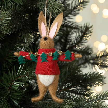 Felt rabbit ornament wearing a red sweater with green trees on a Christmas tree.
