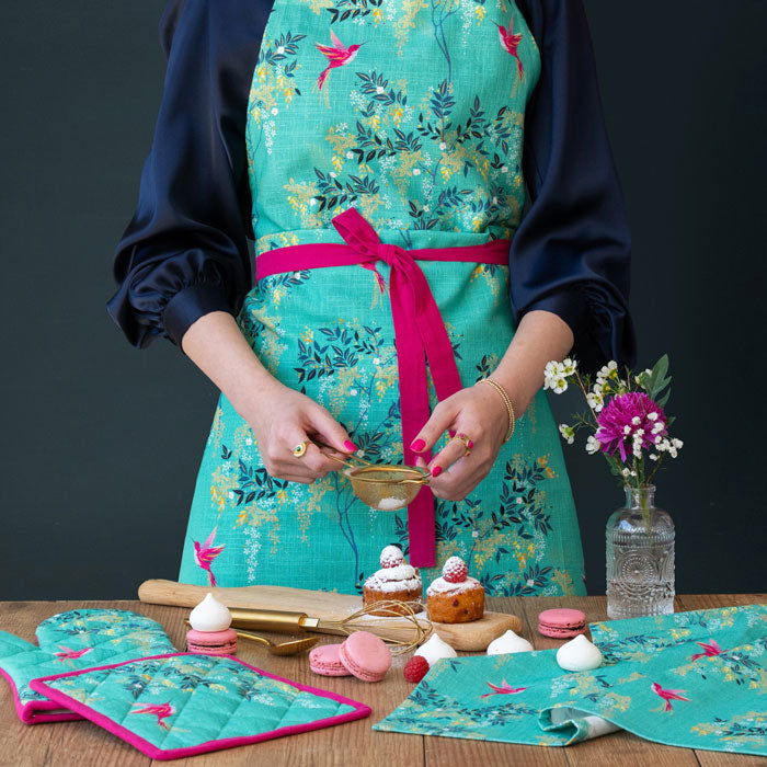 Person wearing a green apron hummingbird and foliage design.