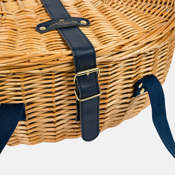 Wicker picnic basket with navy straps and gold buckle on a white background