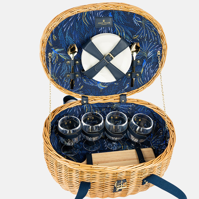 Open picnic basket with blue interior, cutlery, plates, and glasses on a white background
