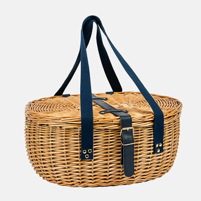 Wicker picnic basket with navy straps on a light gray background