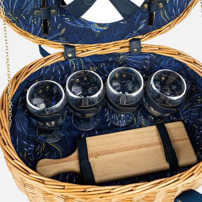 Open picnic basket with wicker exterior and blue interior, containing wine glasses and a wooden cutting board.
