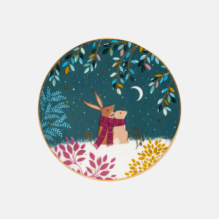 A round decorative coaster featuring a whimsical winter night illustration with two rabbits hugging under a crescent moon, surrounded by colourful leaves and snow.