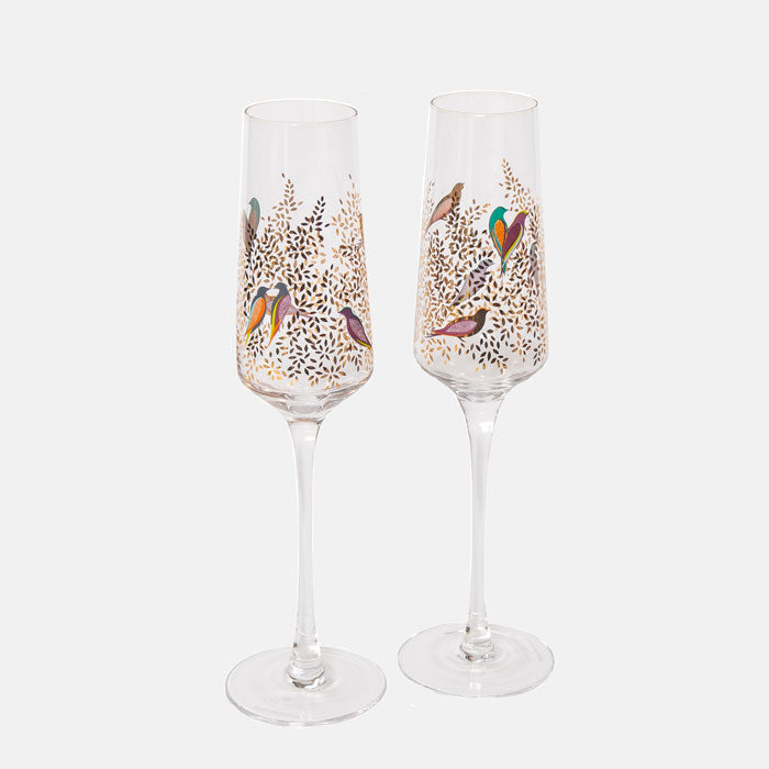 Two champagne flutes with bird and foliage design on a white background