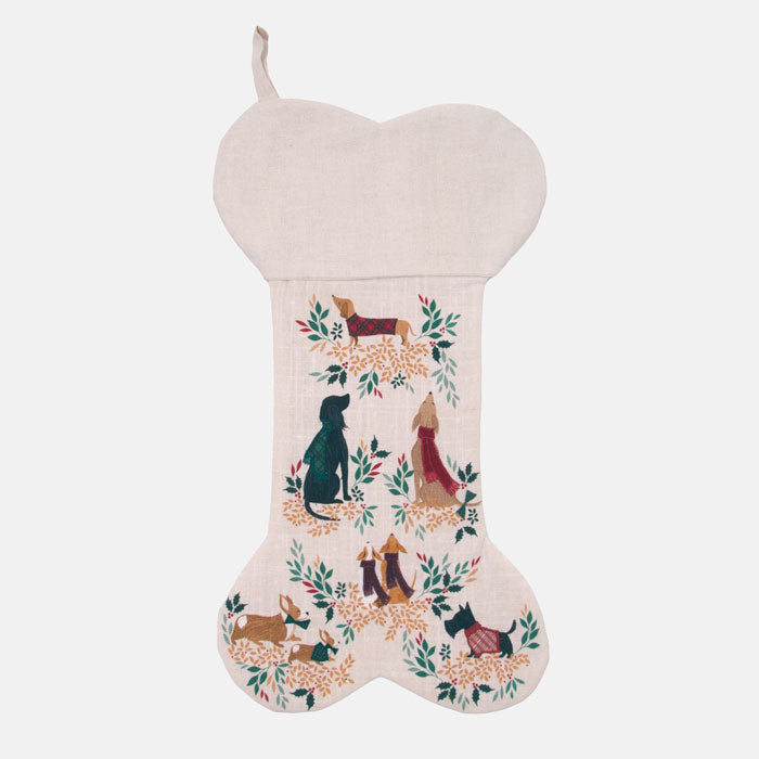 Bone shaped festive stocking with dogs dressed in scarves and jumpers and festive foliage on a cream background.