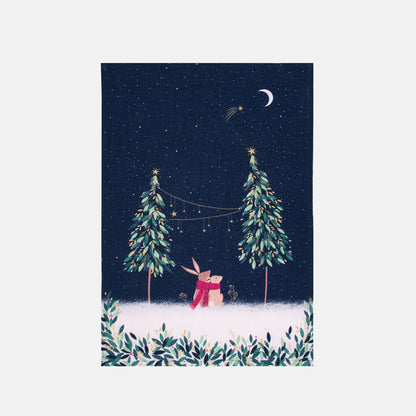Festive tea towel with rabbits in moonlight design, and Christmas trees on a starry sky background.