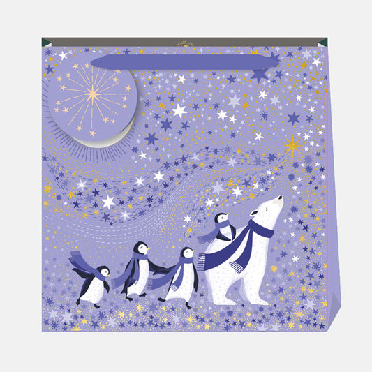 A periwinkle Christmas gift bag with penguins and a polar bear against a starry sky.