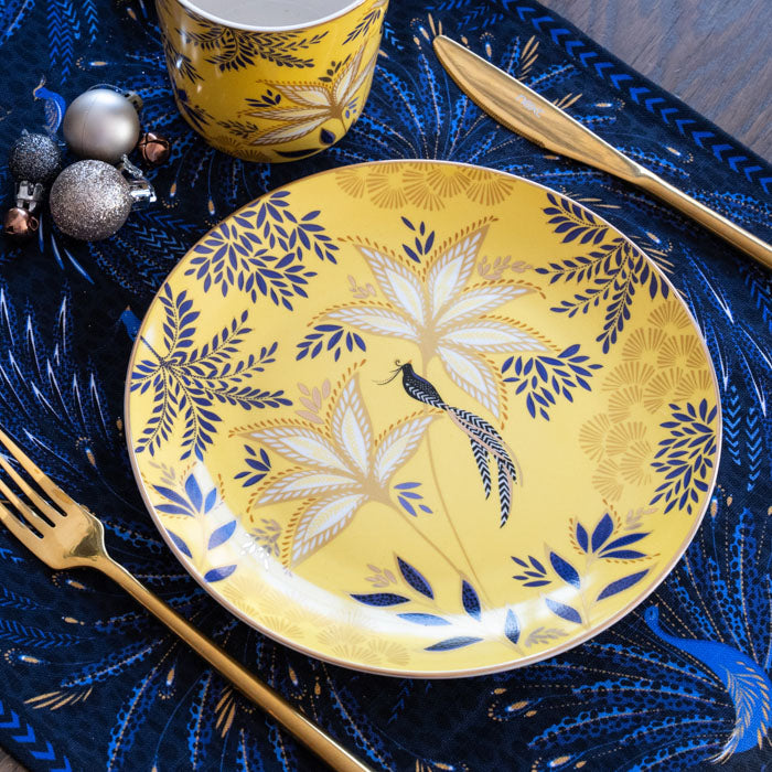 A yellow cake plate with a botanic design and gold embellishment, set on a table with Christmas accents.