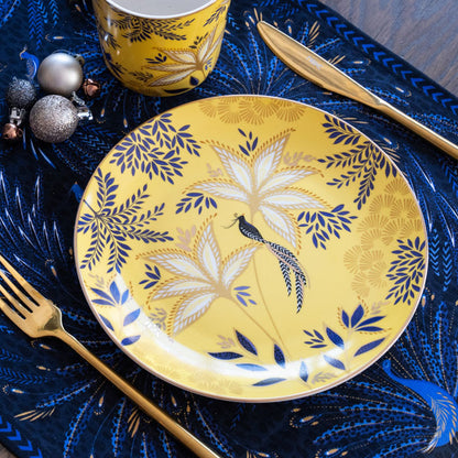 A yellow cake plate with a botanic design and gold embellishment, set on a table with Christmas accents.