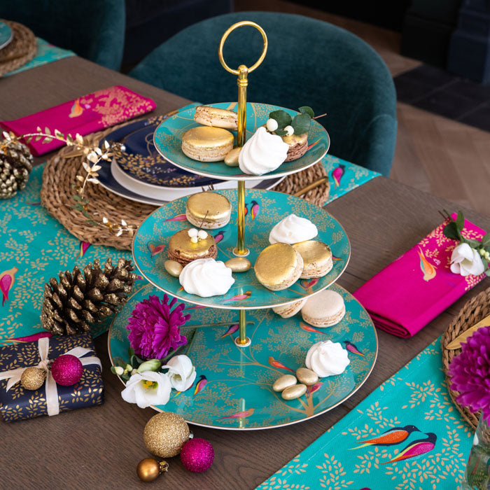 A green cake stand with delicate birds and leaves design, stacked with sweet treats set on a festive table.