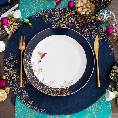 A round navy blue fabric placemat with a hummingbird and foliage design, set on a table with matching plate.