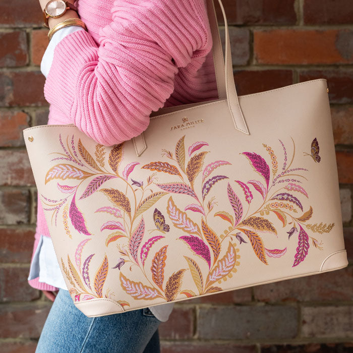 Cream tote style handbag with floral pattern held by a person.