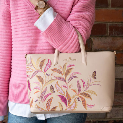 Cream handbag with floral pattern held by a person wearing a pink sweater.