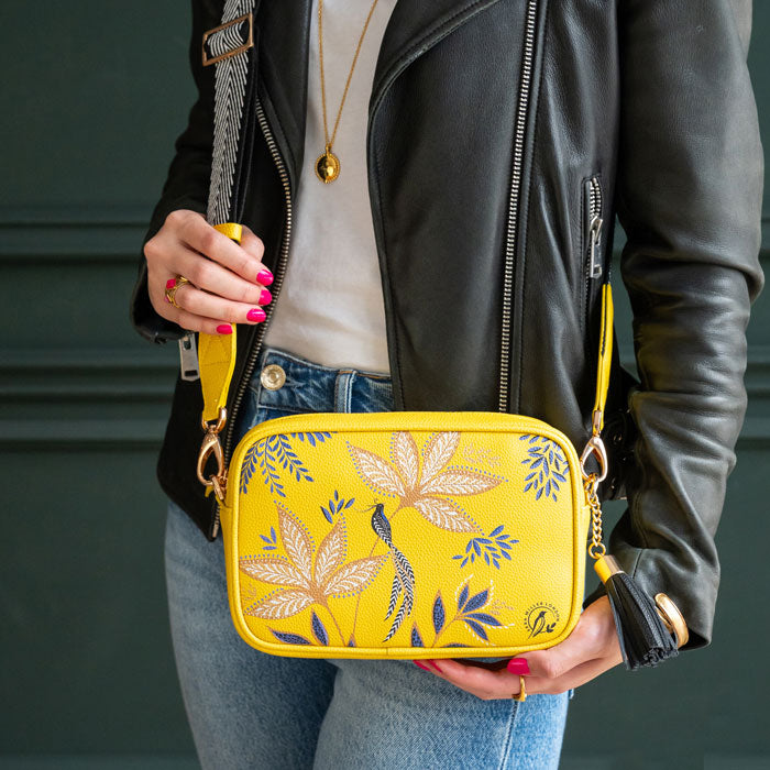 Person holding a yellow crossbody bag with floral design against a dark background
