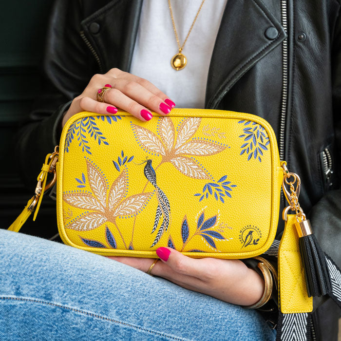 Person holding a yellow crossbody handbag with floral patterns