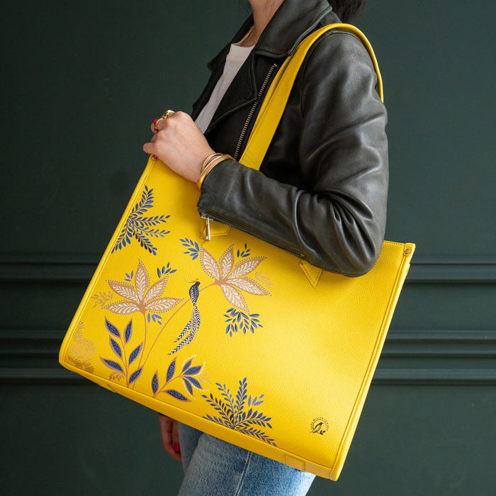 Person holding a yellow tote bag with floral designs against a dark background