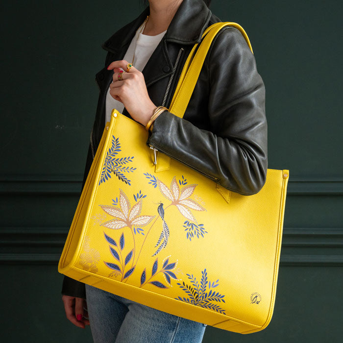 Person holding a yellow bag with floral designs against a dark background