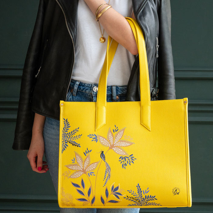Person holding a yellow tote bag with floral designs against a dark background