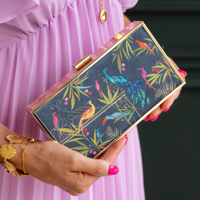 Hand holding a colourful clutch with bird design against a pink dress background