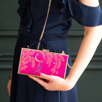 Person holding a pink clutch with gold accents against a dark background