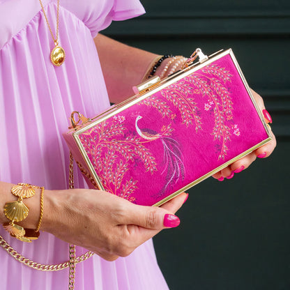 Person holding a pink clutch with gold detailing and peacock design.